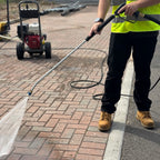 Trigger and lance pressure washing a driveway with a honda powered washer in the background