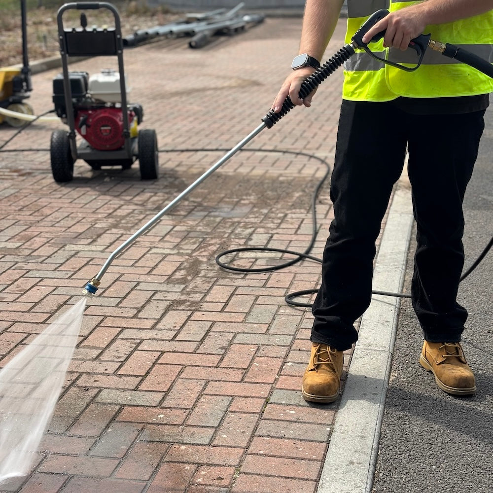 Trigger and lance pressure washing a driveway with a honda powered washer in the background