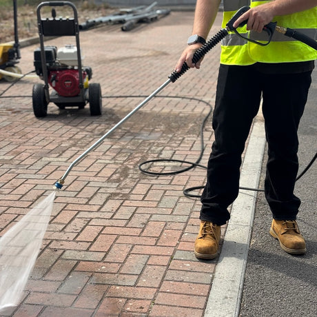 Trigger and lance pressure washing a driveway with a honda powered washer in the background